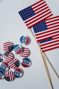 Close-up of American flags and vote buttons on a white backdrop, symbolizing U.S. elections.